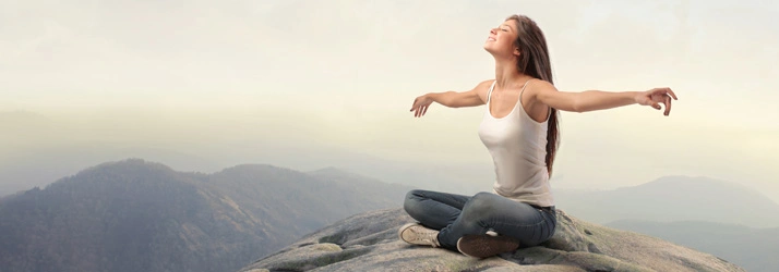 Chiropractic Portland OR Pain Management Person meditating on a mountain peak with arms outstretched, overlooking misty mountains and cloudy sky.